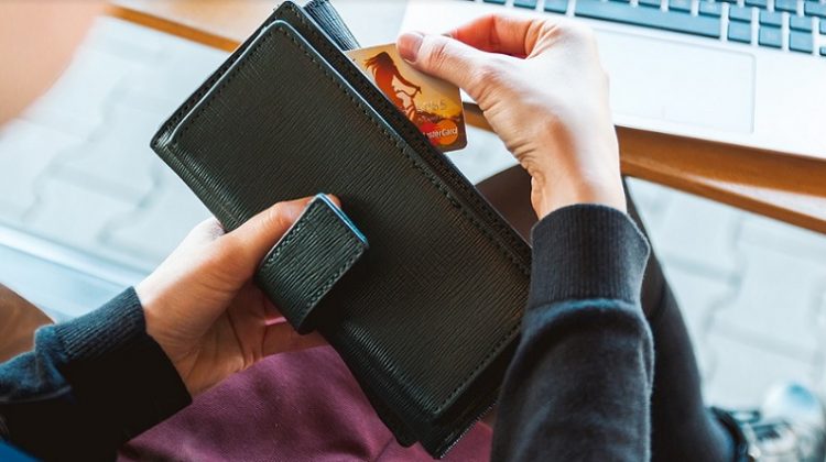 Woman taking a credit card out of a black wallet = Practical Ways To Save Money On Your Household Bills