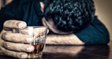 Man with head down on table holding glass of liquor - Alcohol Addiction