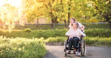 Young woman pushing an older women in a wheelchair down a path in a park -Medicare if You Have ALS or ESRD