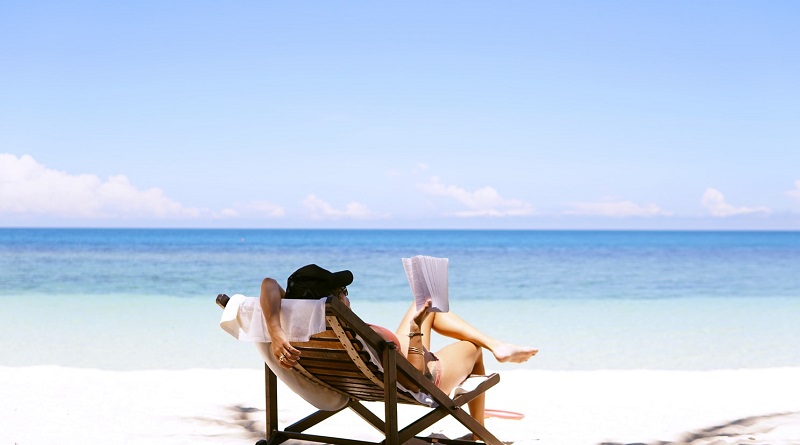 Woman reading in lounge chair on beach - Signs You Need a Holiday