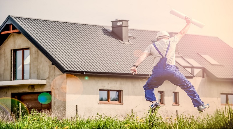 Man in overalls holding building plans, jumping in air in front of house - Your Dream Home