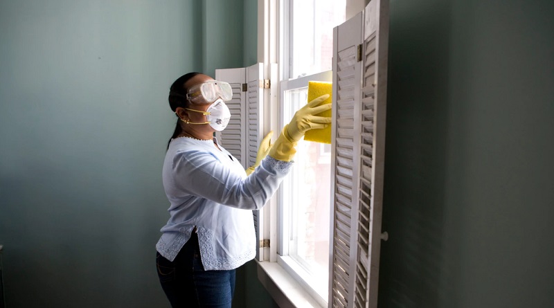 Woman in mask and goggles, cleaning a window