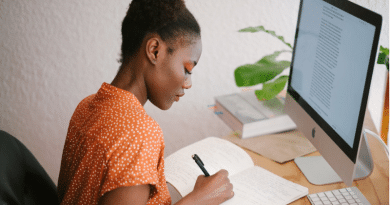 Young woman sitting at desk with computer writing in notebook Online Degree