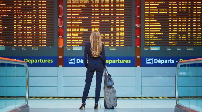 Ways to Dress Up Woman wearing a pantsuit and heels, with roller bag luggage at airport