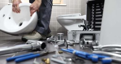 Plumber holding sink surrounded by tools and supplies on the floor around his feet
