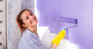 Add Value To Your Home Woman wearing yellow rubber gloves roller painting a wall purple