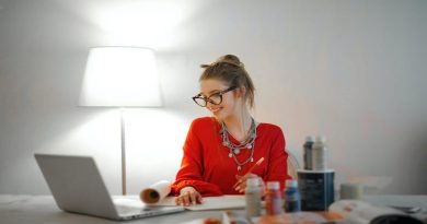 Ideas To Follow Your Passion / Woman in Red Dress at Work Table with Paints Sketchbook and Laptop
