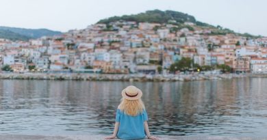 Wardrobe Essentials for Traveling in Southern Europe / Woman Sitting at the side of the water overlooking a small town.