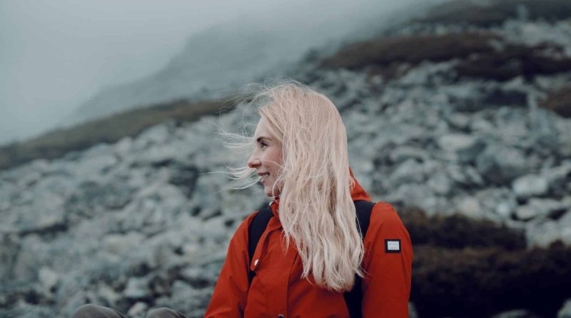 Woman with blonde hair wearing a red jacket sitting on a rocky hillside