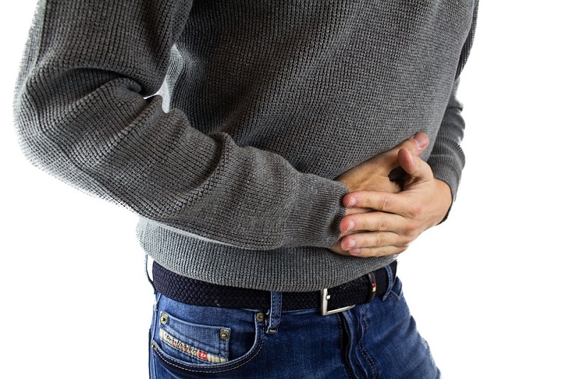 Man in Jeans and Grey Sweater holding his painful stomach