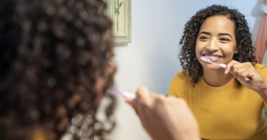 Healthy Gums & Teeth / Young woman with curly hair wearing a yellow top brushing her teeth