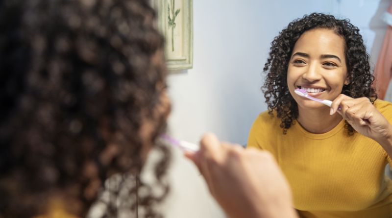 Healthy Gums & Teeth / Young woman with curly hair wearing a yellow top brushing her teeth