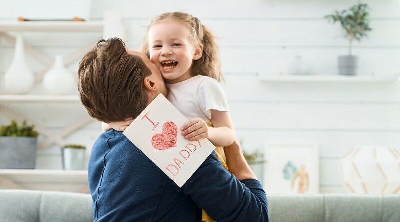 Dad hugging his smiling little girl who is holding a Father's Day card