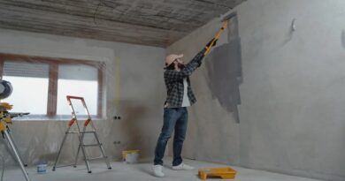 Affordable Improvements / Man in jeans, plaid shirt and baseball cap painting bare concrete walls