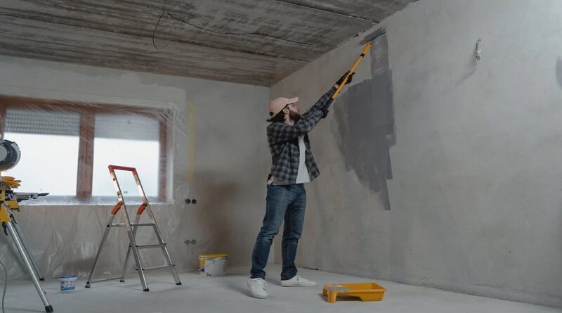 Affordable Improvements / Man in jeans, plaid shirt and baseball cap painting bare concrete walls