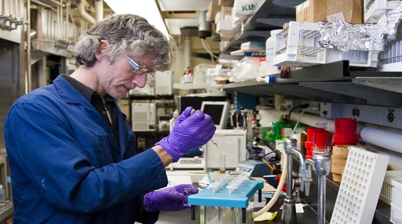 Researcher in Blue Lab Coat Wearing Purple Gloves and Safety Goggles Doing Lab Work
