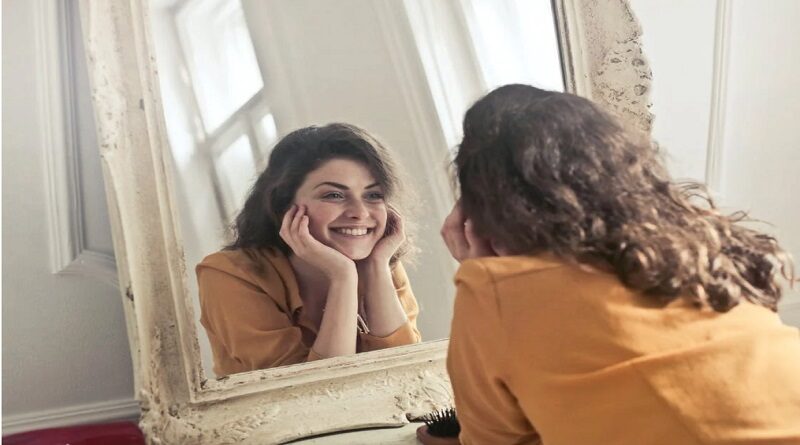 Practicing Self Acceptance and Self Care / Smiling brunette woman looking at herself in a antique framed mirror