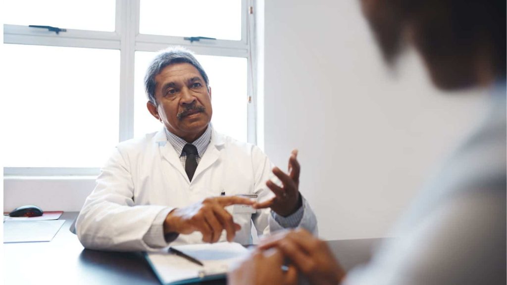 Restoring Your Health After A Car Accident Injury / Dr. in a shirt tie and white coat at his desk speaking to a patient
