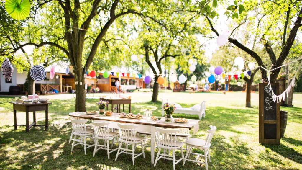 Large white table with chairs in a back yard decorated for a party