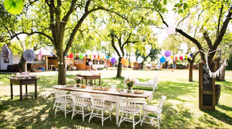 Large white table with chairs in a back yard decorated for a party