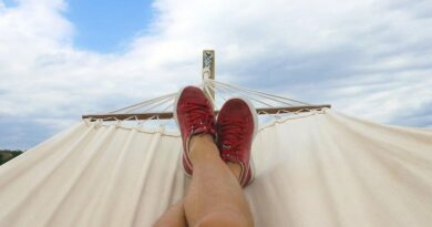 Mans legs and feet in red sneakers laying in a hammock under a blue and cloud filled sky