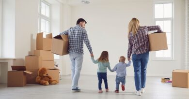 Discover The Average Cost Of Moving House / A couple holding hands with 2 small children while carrying moving boxes through an almost empty room
