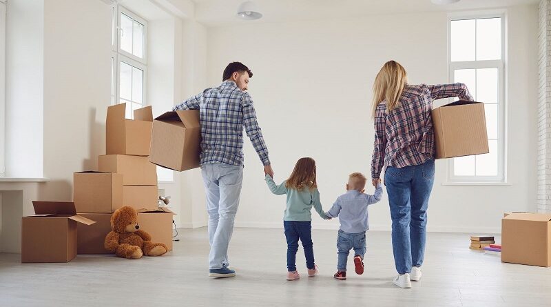 Discover The Average Cost Of Moving House / A couple holding hands with 2 small children while carrying moving boxes through an almost empty room
