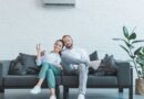 Couple Sitting On a Gray Sofa Underneath a Central Air Conditioning Unit
