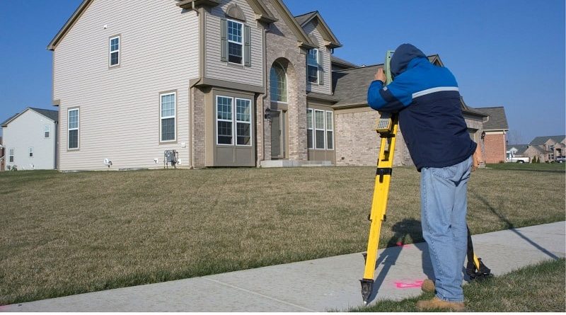 Property Survey / Man surveying property of a 2 story beige brick home