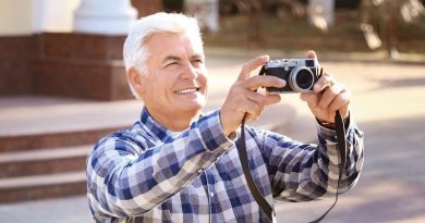 Older man with white hair wearing a blue and white check shirt looking through a camera