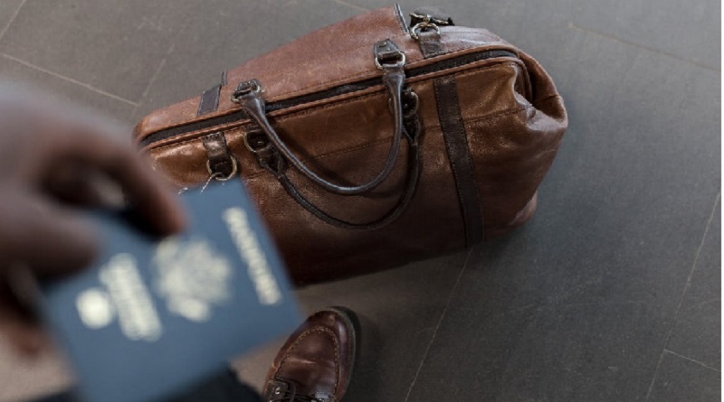 Man holding a passport with a travel duffle at his feet / How to Make the Most out of Work-Related Travel