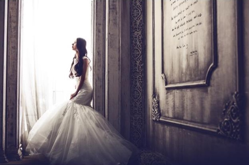 Bride in Wedding Gown standing by a window