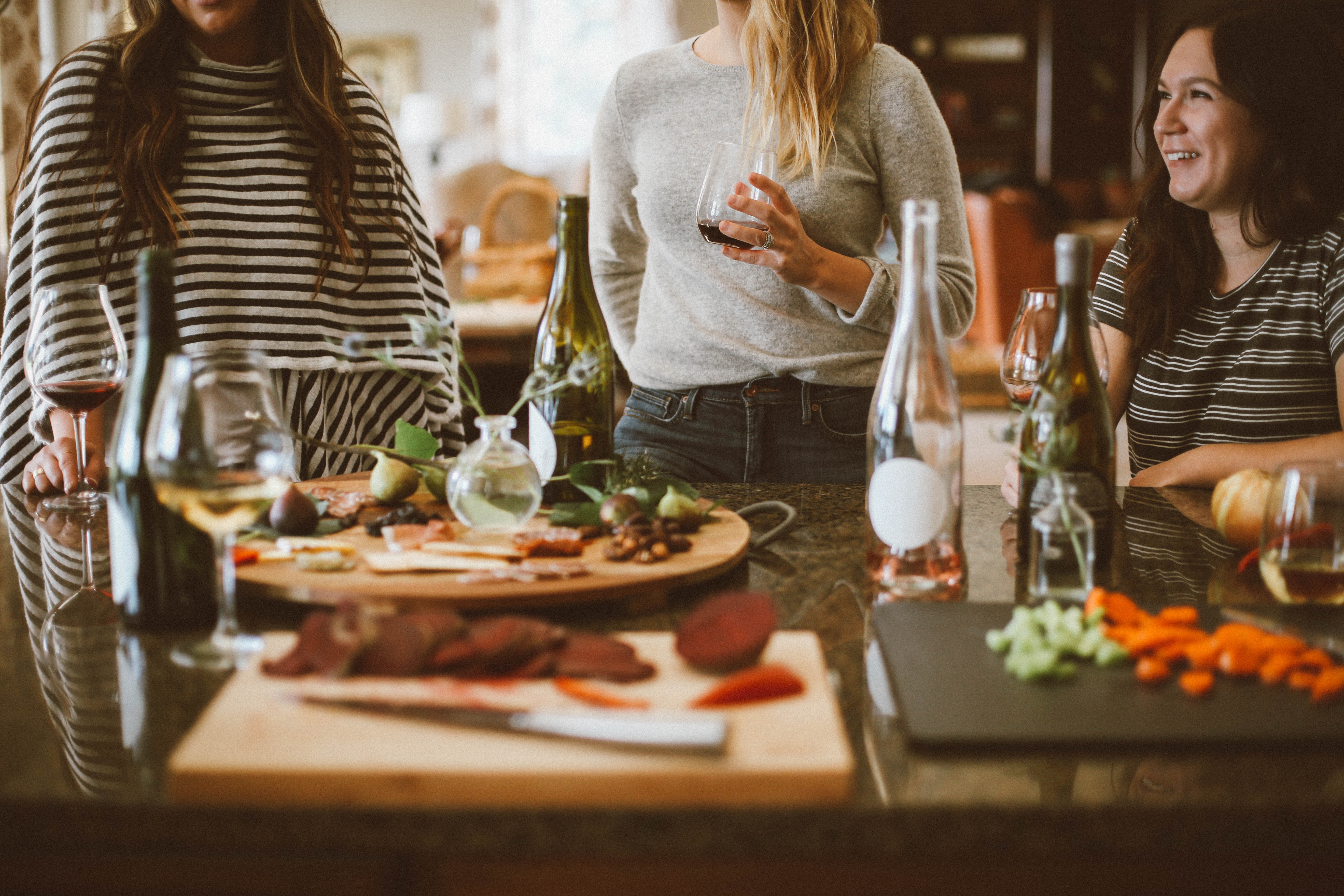 A Guide To Planning the Ultimate Office Christmas Party / Three Women Drinking Wine at a Food Table at a Party