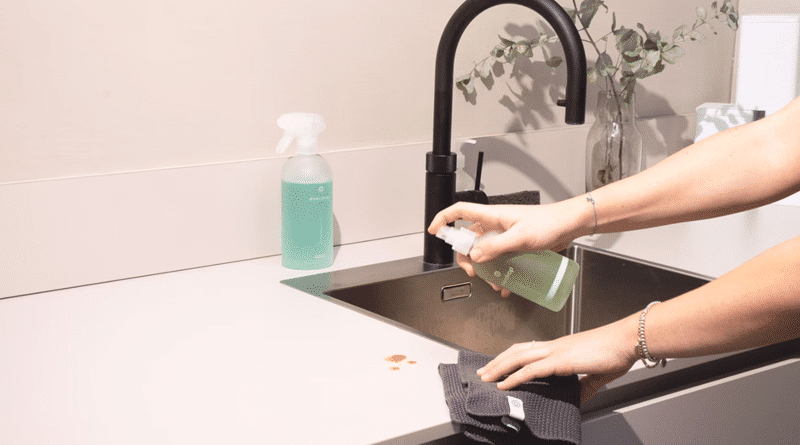 Woman Spraying Kitchen Counter / Important Home Maintenance Tasks to Tackle Sooner Rather Than Later