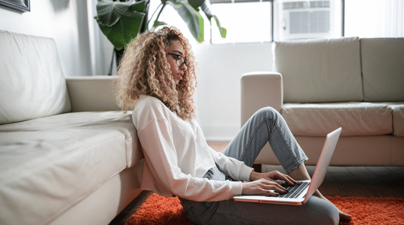 Woman sitting on orange rug leaning against a white sofa working on her laptop / Important Warranties Every Homeowner Should Have